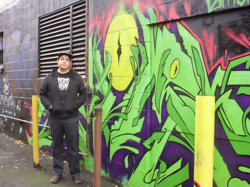 Rico Alvarez standing in front his graffiti art