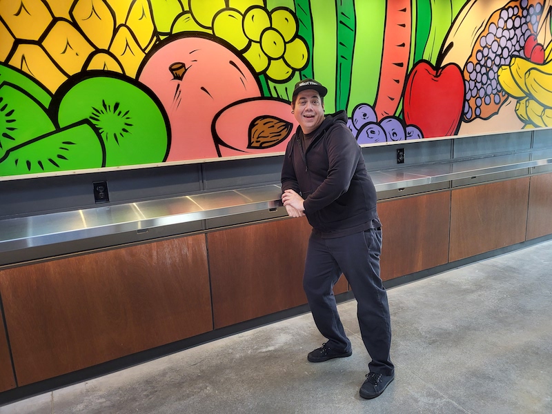 Rico Alvarez in front of his fruit mural hanging in Rockwood Marketplace.