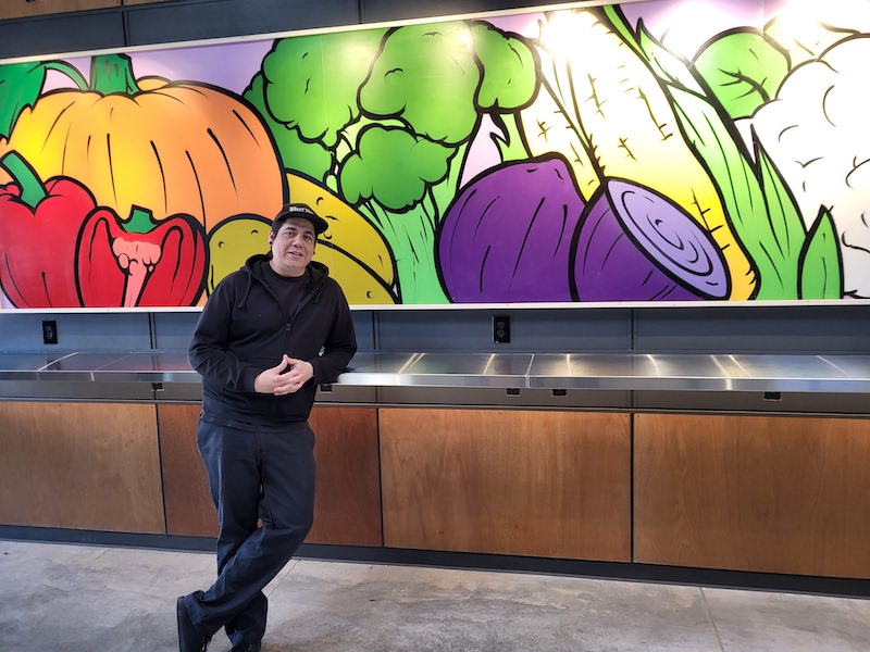 Rico standing in front of his vegetables mural
